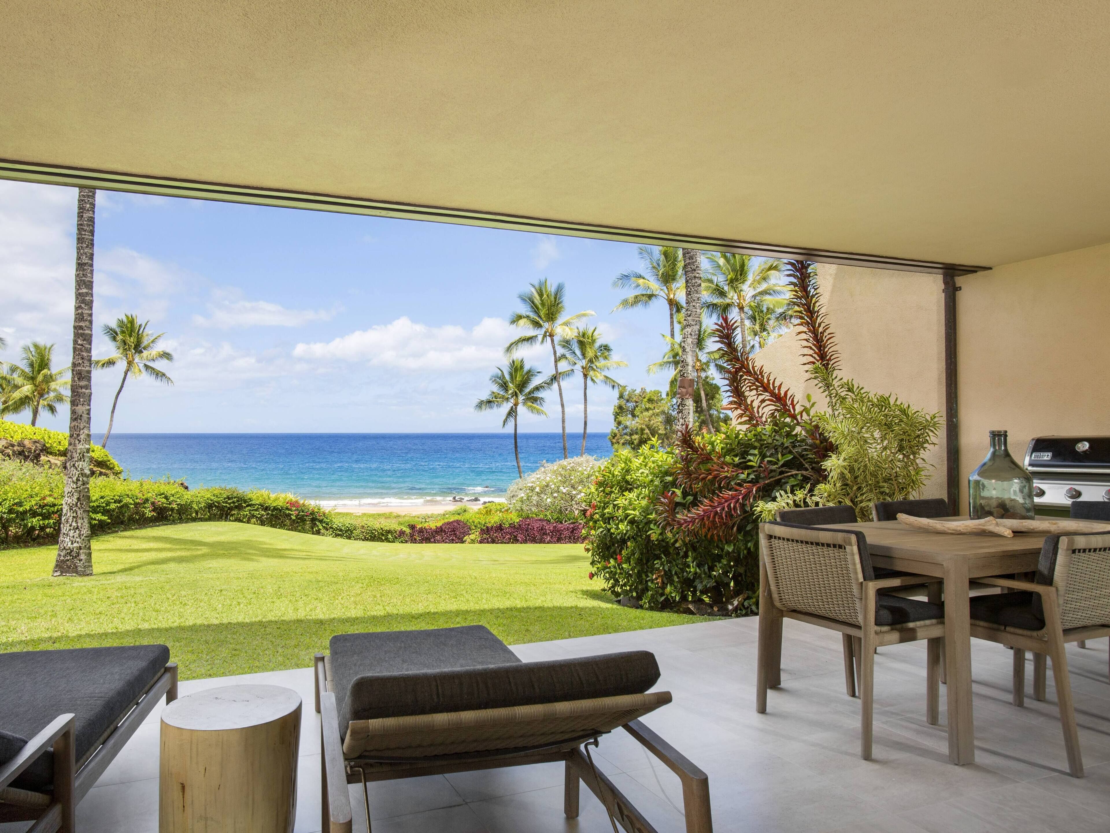 Un patio frente a la playa con vista al océano, una parrilla y mobiliario de exterior.
