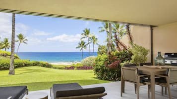 Un patio frente a la playa con vista al océano, una parrilla y mobiliario de exterior.
