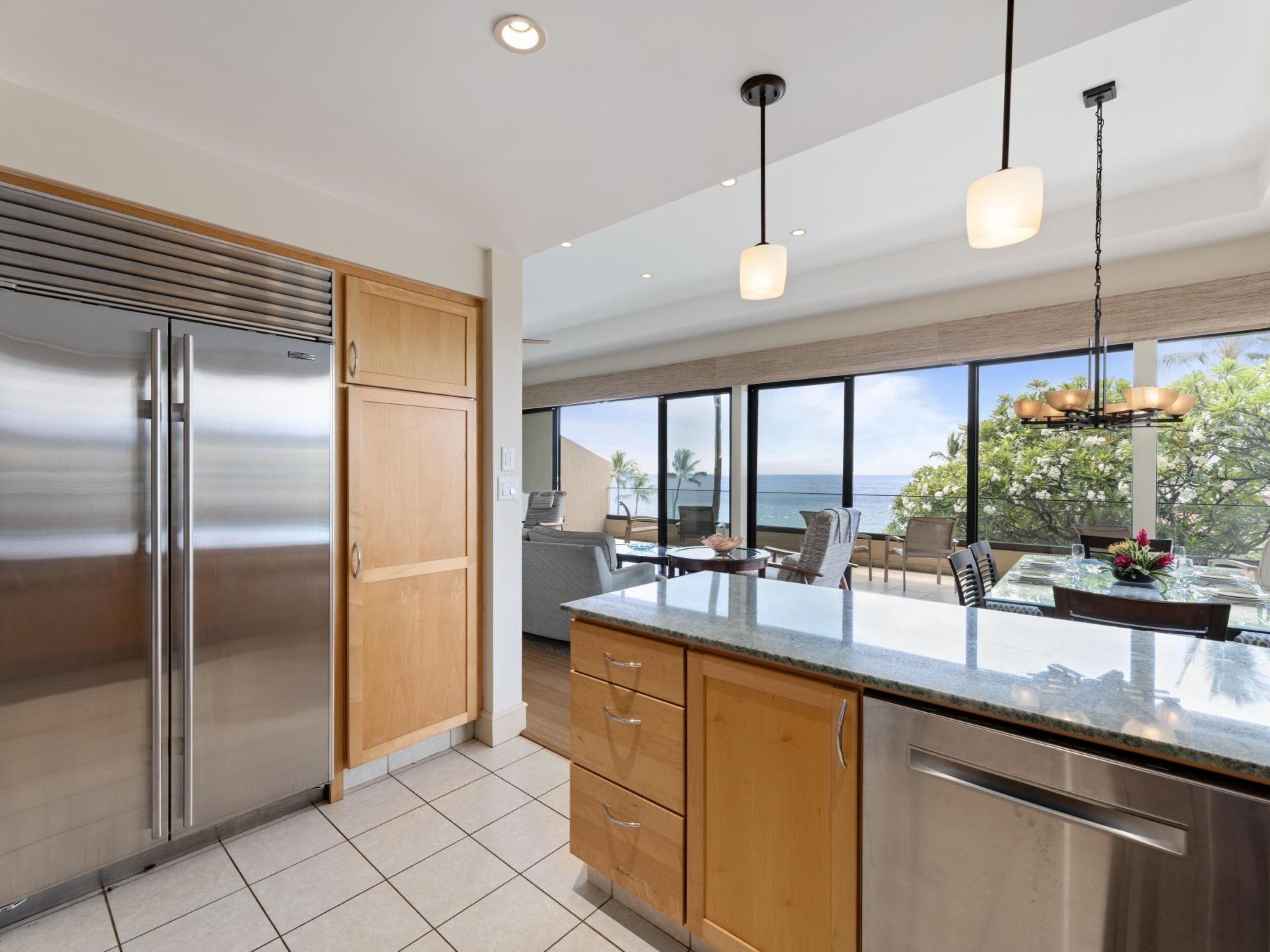 A modern kitchen with a large island, stainless steel appliances, wooden cabinets, and a view of the ocean.