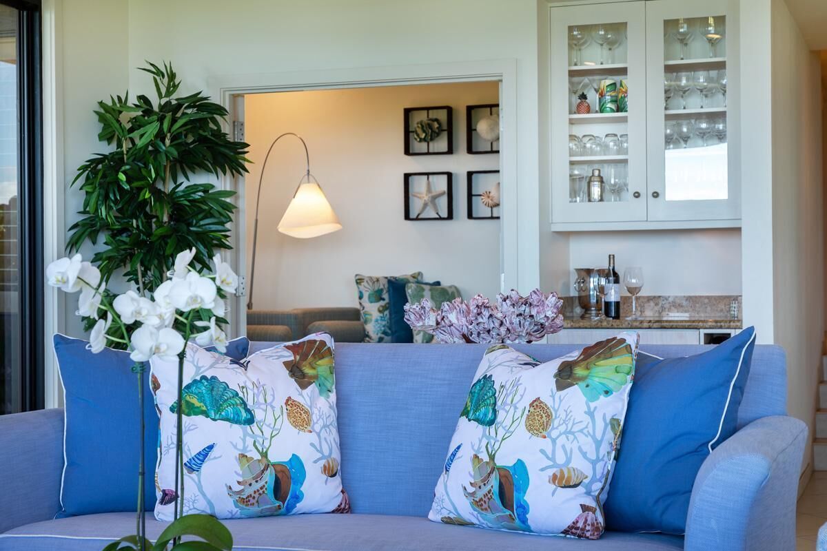 A living room with a blue sofa, decorative pillows, a potted plant, and a cabinet with glassware.