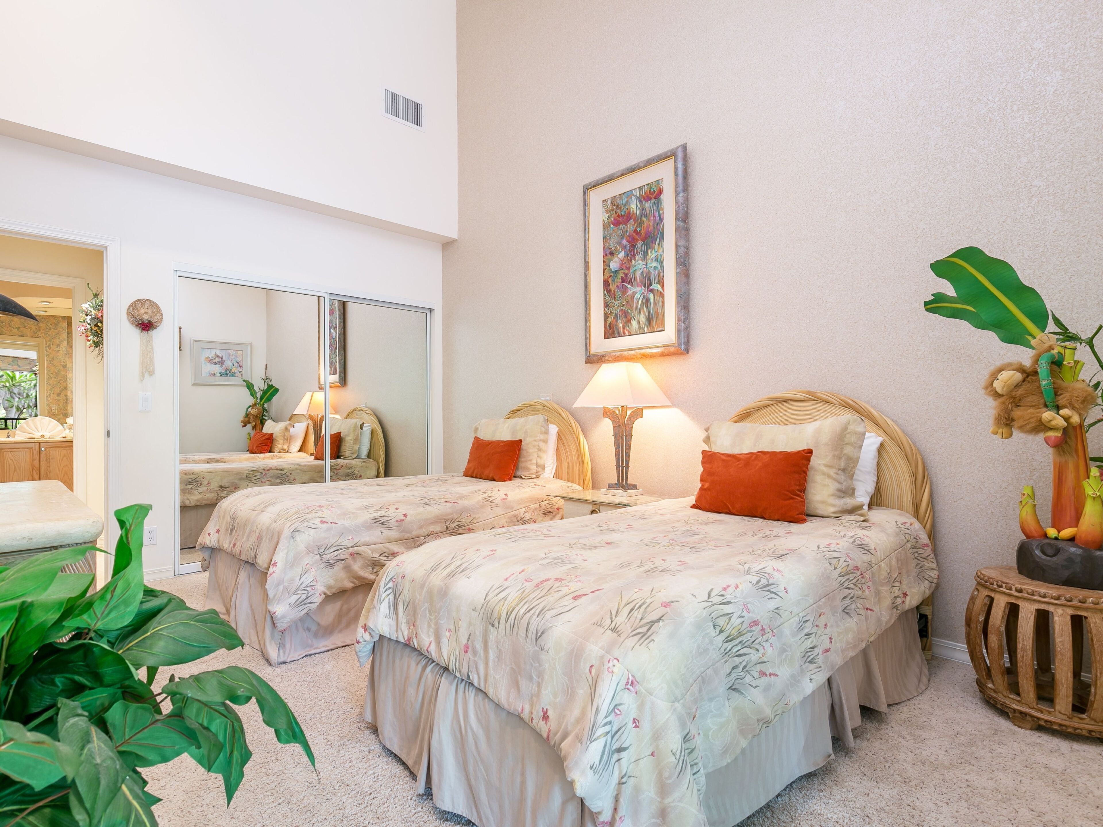 A hotel room with two beds, a large mirror, a painting, and a small side table with a plant.