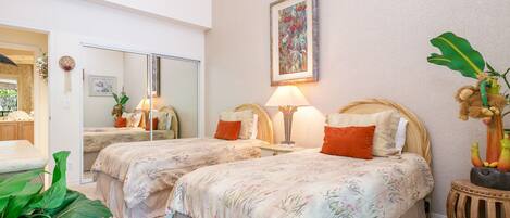 A hotel room with two beds, a large mirror, a painting, and a small side table with a plant.