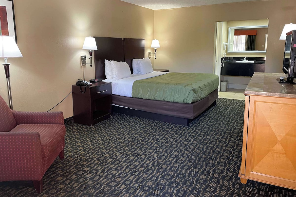 A hotel room with a bed, bedside lamps, a desk, a chair, and a television.