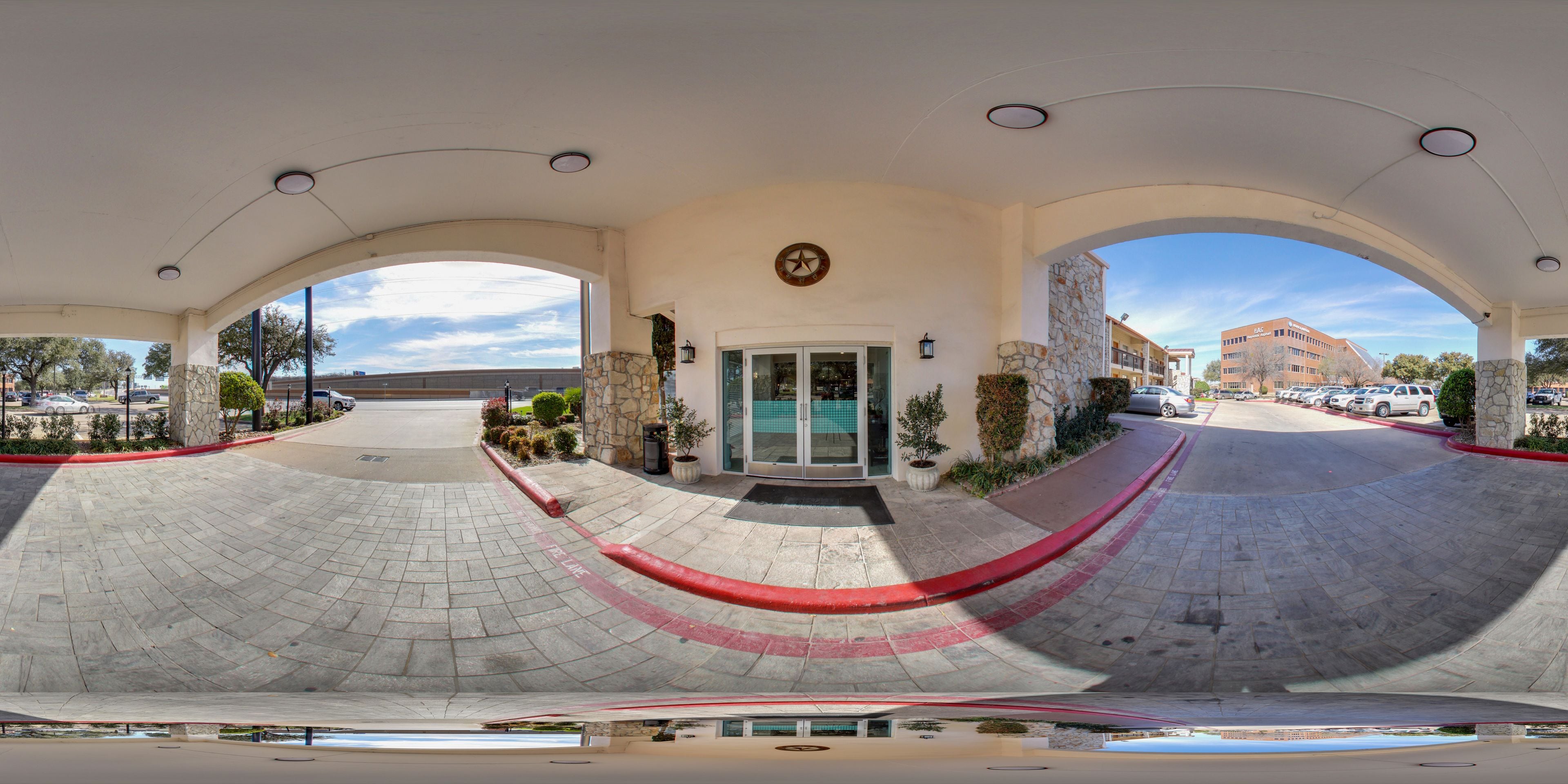 A hotel entrance with a curved driveway, stone pillars, and a clear sky.