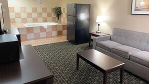 Une chambre d’hôtel avec un canapé, une petite table, un réfrigérateur, une lampe, un lavabo et un mur recouvert de carreaux.