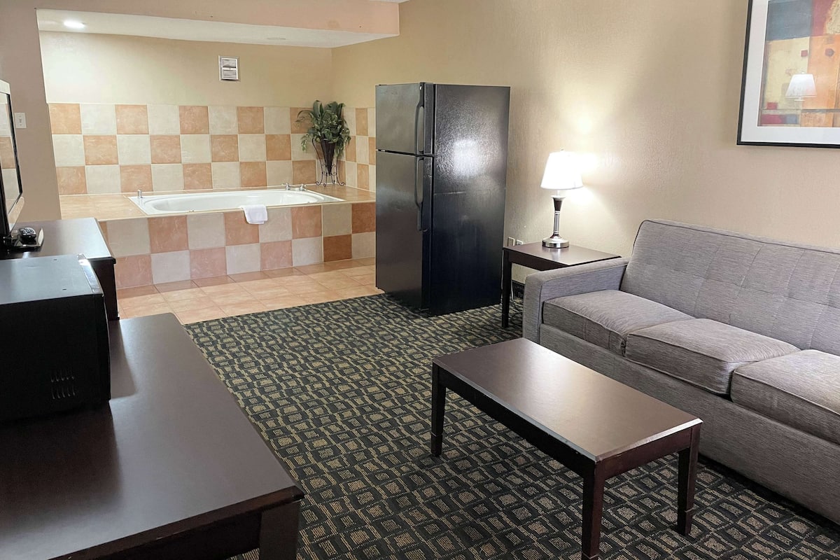 A hotel room with a sofa, a small table, a refrigerator, a lamp, a sink, and a tiled wall.