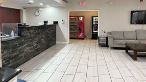 Un espace d’accueil comprenant un comptoir de réception, une horloge, un distributeur automatique de Coca-Cola, un téléviseur et un canapé.