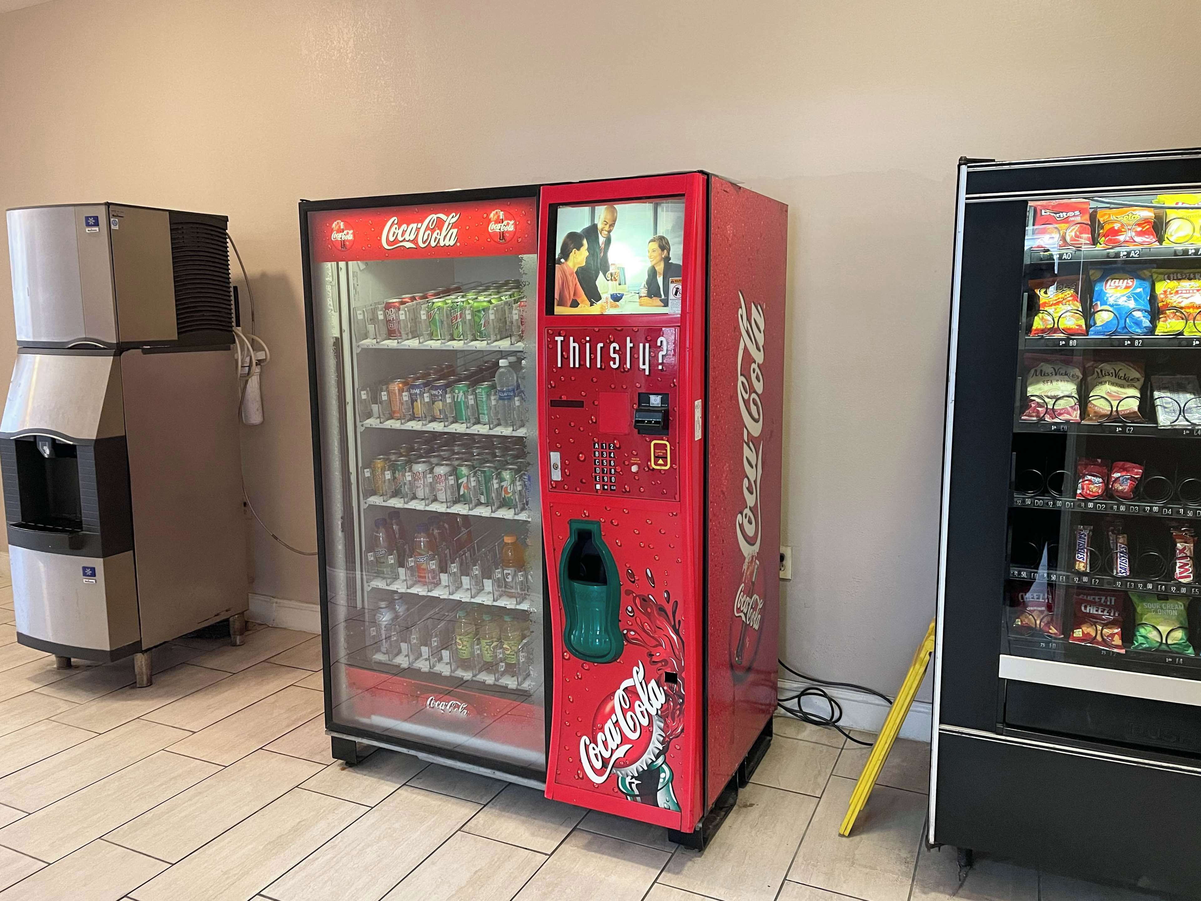 Una máquina expendedora con publicidad de Coca-Cola, un dispensador de agua y otra máquina expendedora de aperitivos.
