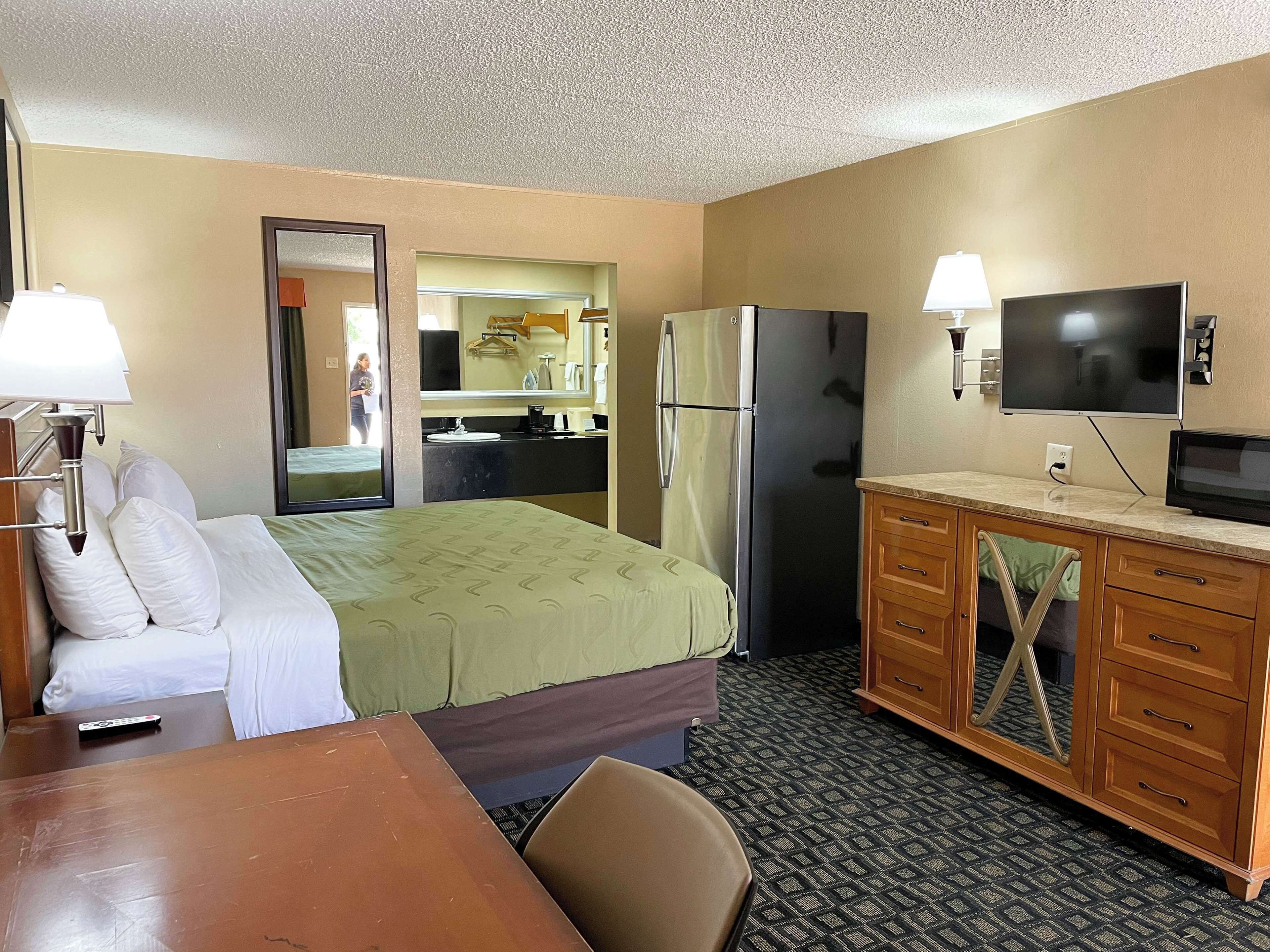 A hotel room with a bed, a desk, a refrigerator, a television, and a bathroom visible through an open door.