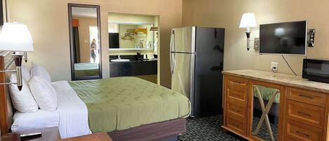 A hotel room with a bed, a desk, a refrigerator, a television, and a bathroom visible through an open door.
