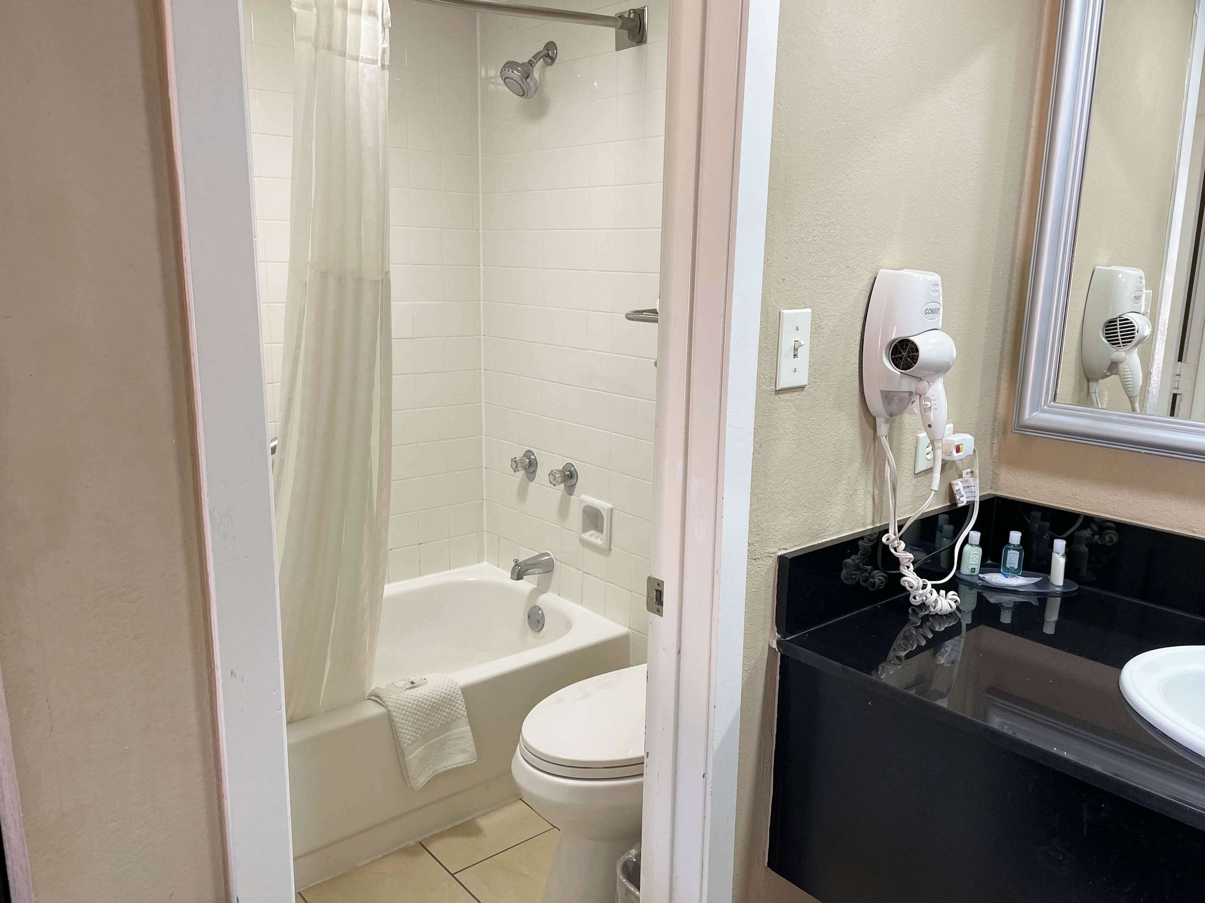 Une salle de bain équipée d’une baignoire, de toilettes et d’un meuble-lavabo avec un miroir et un sèche-cheveux.
