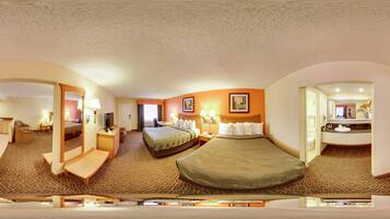 A hotel room with a bed, desk, chair, and a bathroom with a sink and mirror.