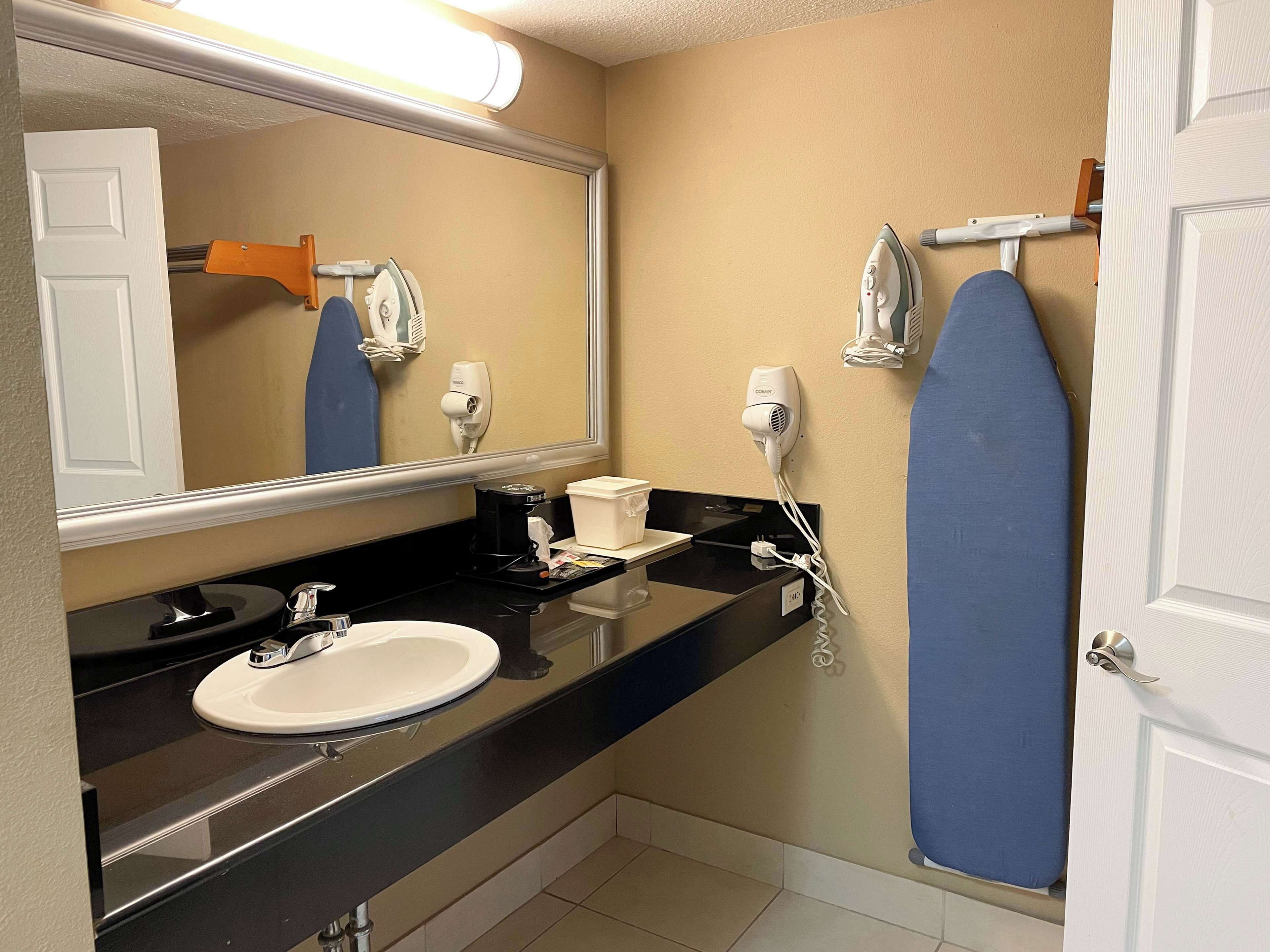 Un baño con lavamanos, espejo y dos secadores de pelo fijados en la pared.