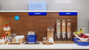 A breakfast bar with labeled sections for cereal and fruit, a kettle, and condiments. - Holiday Inn Express & Suites Annapolis by IHG (Annapolis)