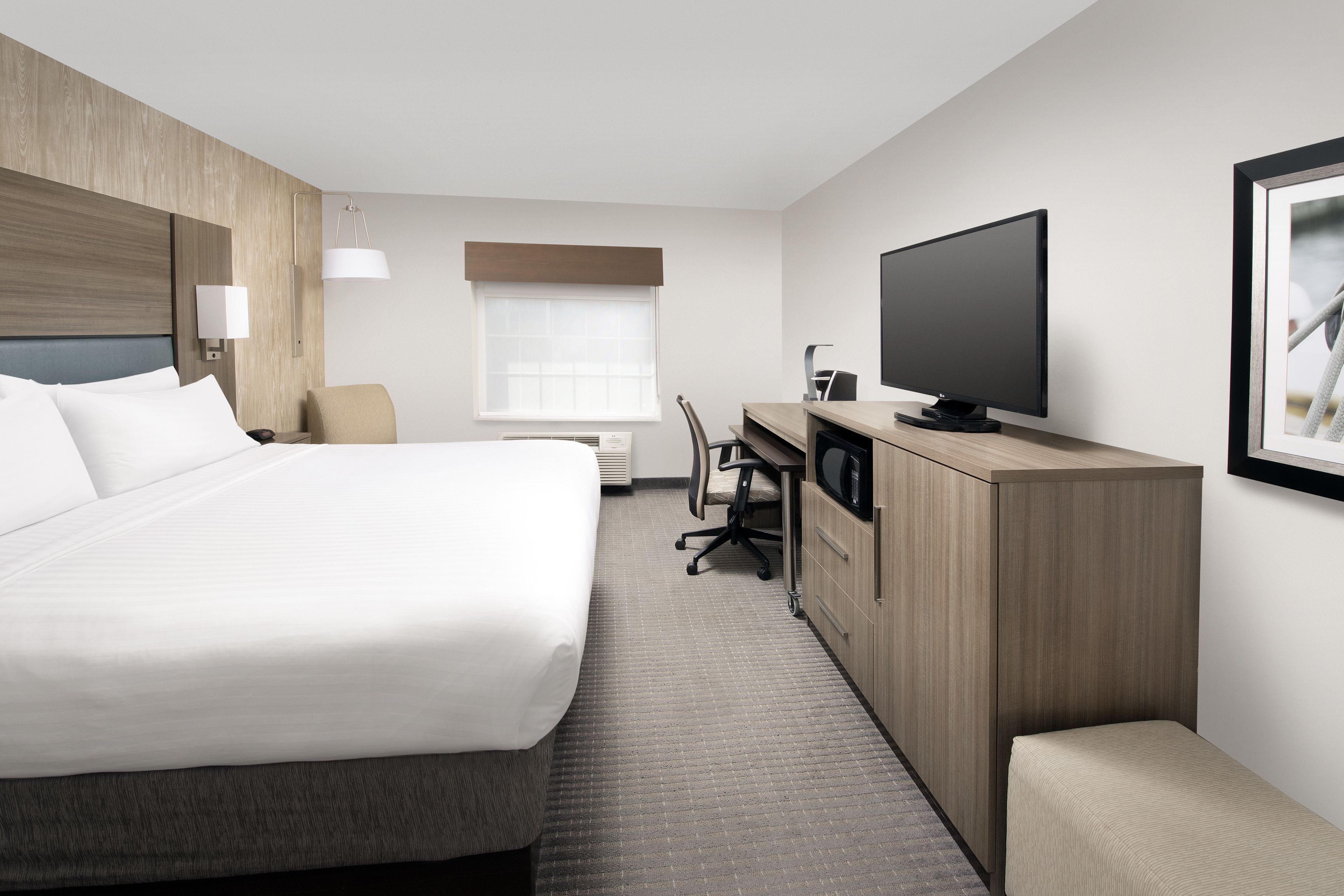 A hotel room with a large bed, a desk, a chair, a television, and a window.