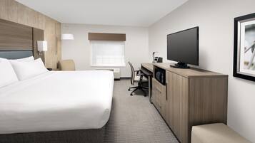 A hotel room with a large bed, a desk, a chair, a television, and a window.