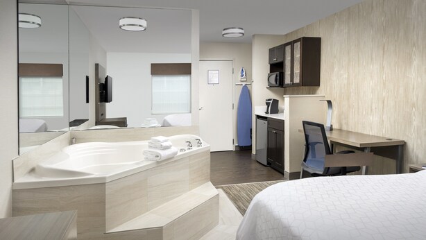 Habitació d'hotel moderna amb un llit gran, un bany separat amb banyera, escriptori i microones.