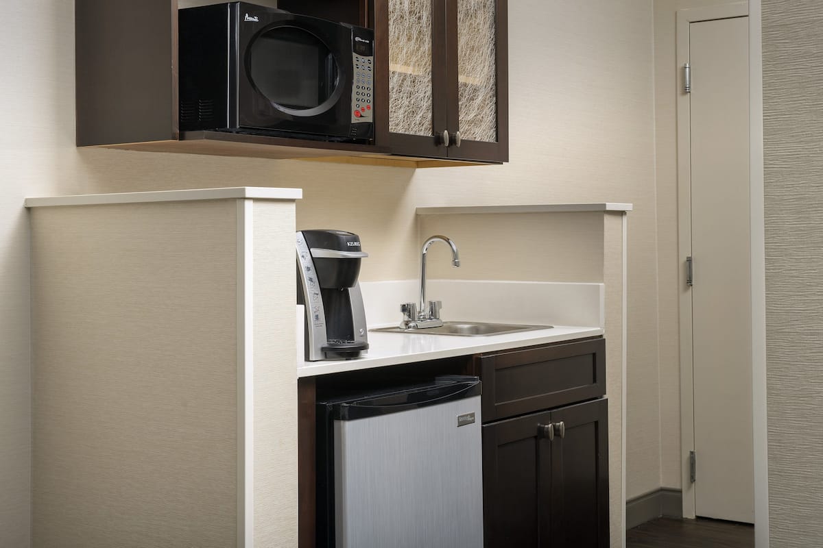A compact kitchenette with a microwave, coffee maker, sink, and a dishwasher.