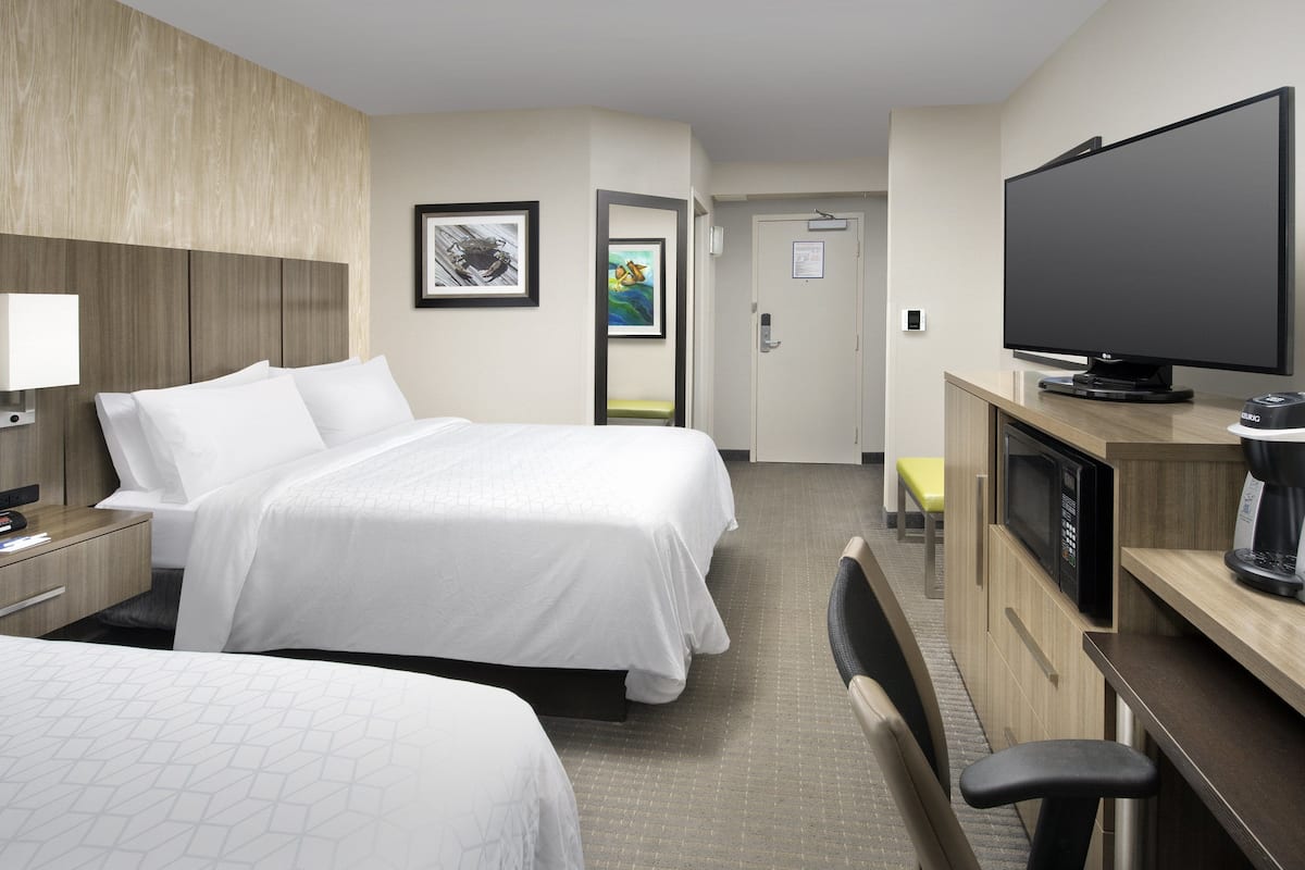A hotel room with two beds, a TV, a microwave, and a desk with a chair.