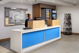 Una recepción de hotel con un quiosco digital, un refrigerador lleno de bebidas y un dispensador de bebidas de autoservicio.