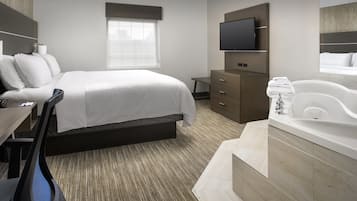 A modern hotel room with a large bed, a flat-screen TV, a bathroom with a bathtub, and a desk with a chair.