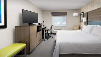 A hotel room with a bed, a desk with a computer, a television, a bench, and a window with a view.