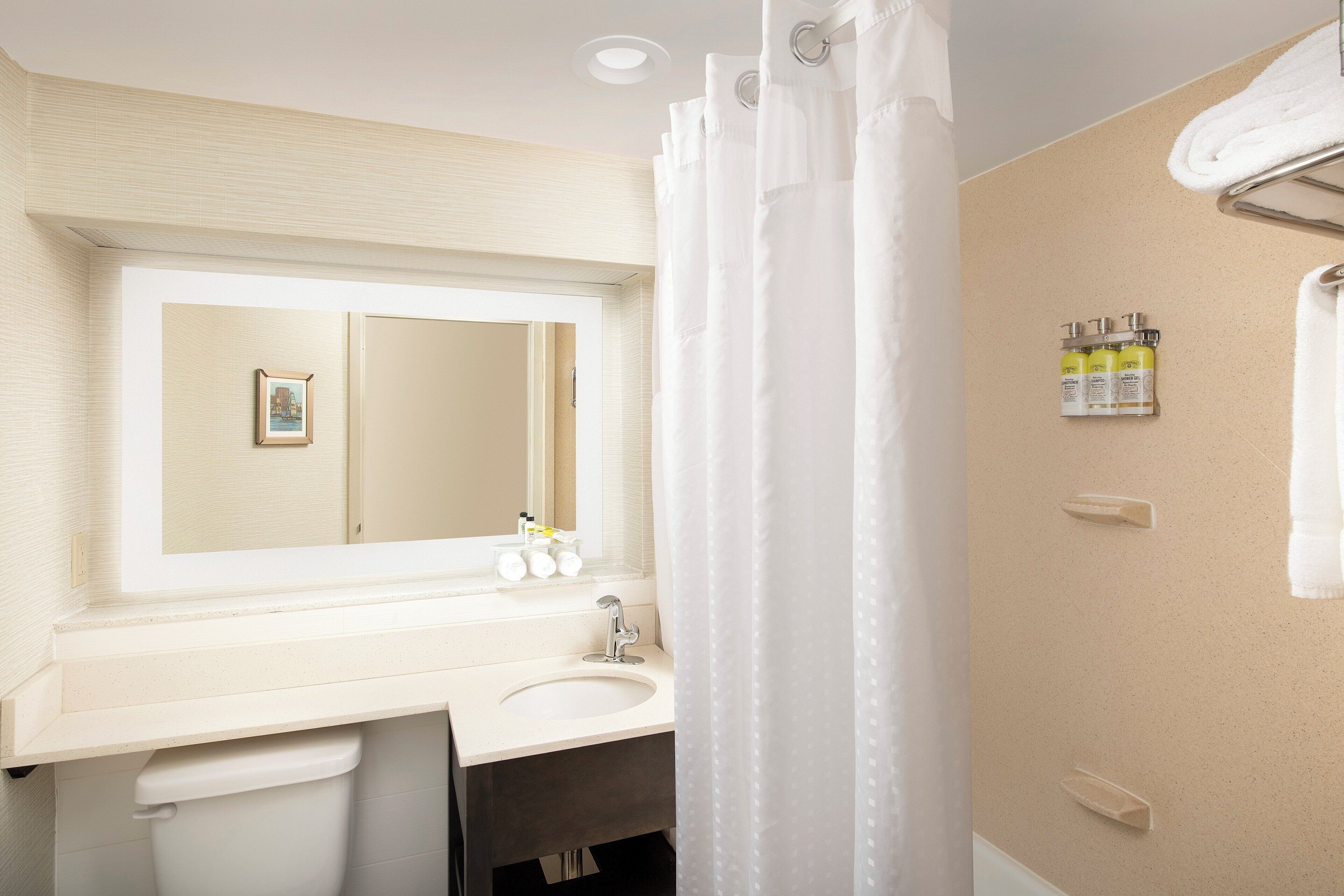 A bathroom with a white sink, mirror, and shower curtain. There are toiletries on the wall and a towel rack.