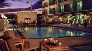 A pool area with lounge chairs and a table with candles, surrounded by a building with balconies and a stone wall. - Courtyard by Marriott Los Angeles - Sherman Oaks (Sherman Oaks)