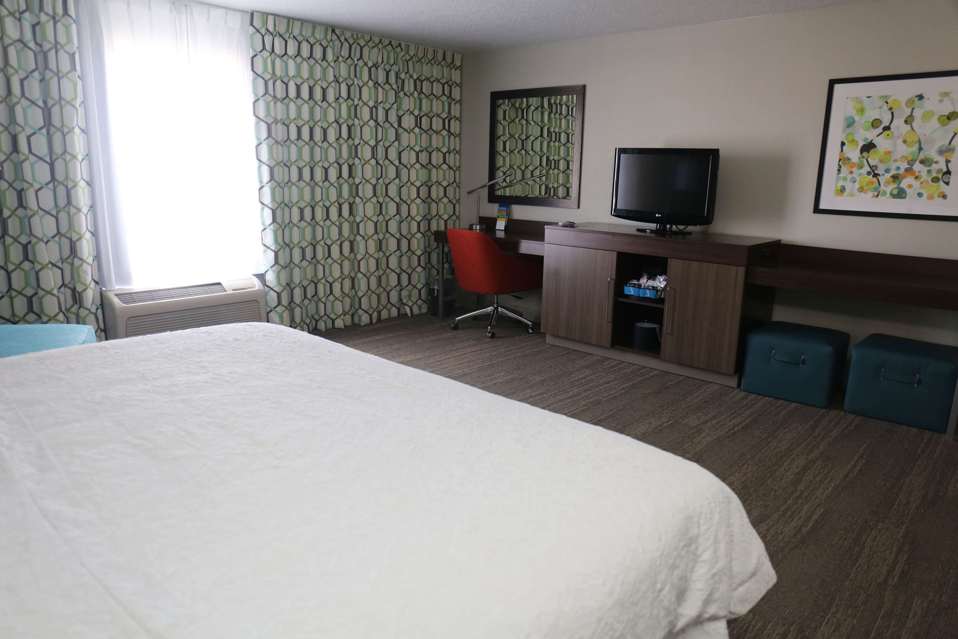 Habitación de hotel con una cama grande, un escritorio con computadora, televisor y una silla.