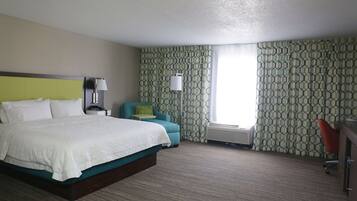 A hotel room with a large bed, a desk, a chair, and a window with patterned curtains.