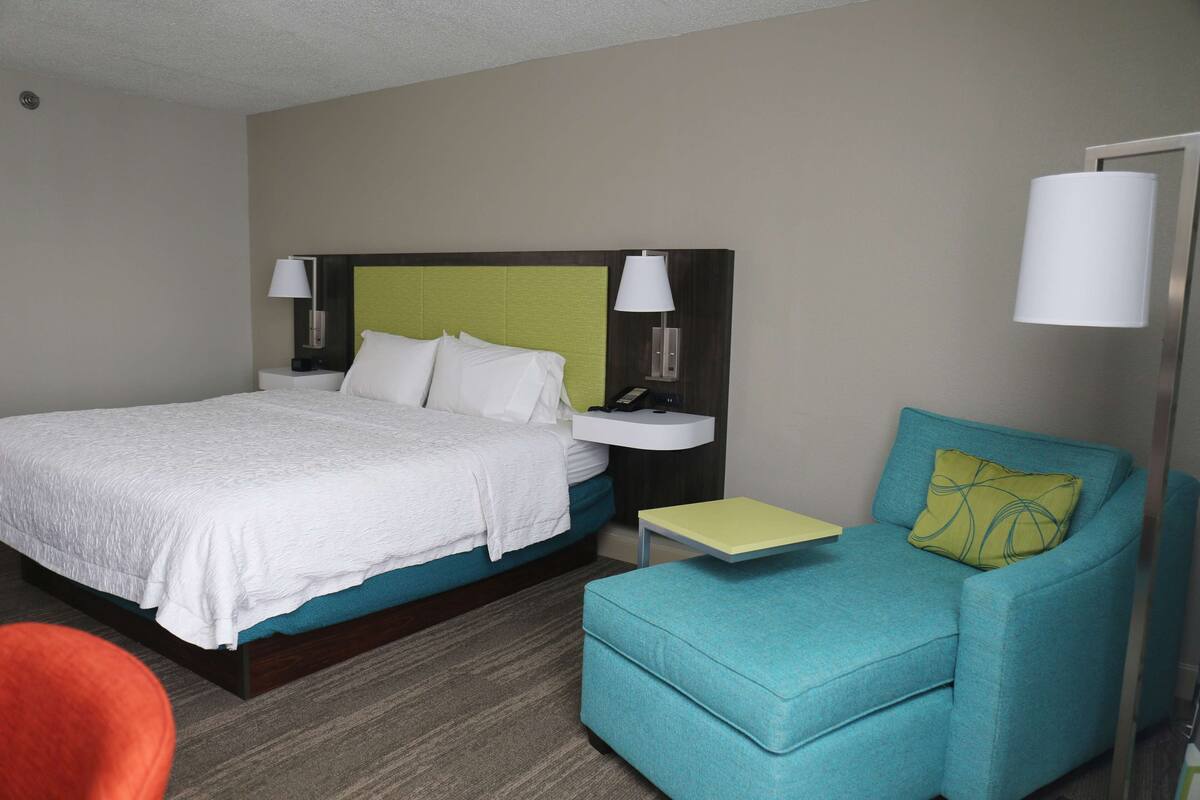 A hotel room with a bed, a nightstand, a chair, and a lamp.