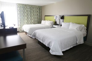 A hotel room with two beds, a desk, a TV, and a patterned curtain.