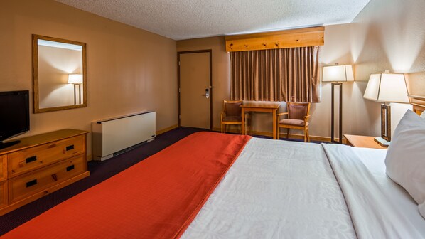 A hotel room with a bed, a desk, a chair, a television, and a window with curtains.