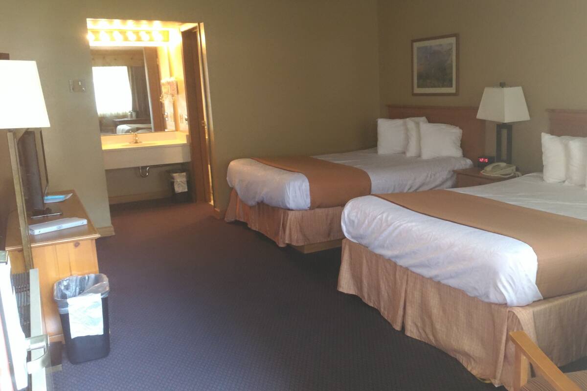 A hotel room with two beds, a bathroom, a desk with a lamp, and a TV.