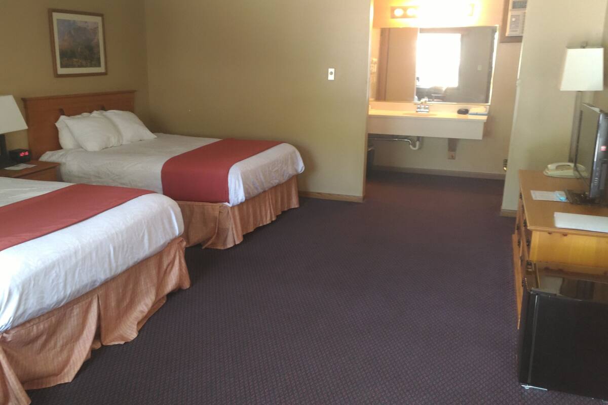 A hotel room with two beds, a desk, a mirror, and a nightstand.