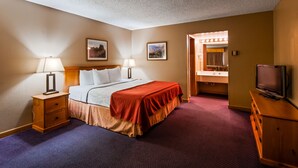 A hotel room with a bed, bedside lamps, a television, a mirror, and two framed pictures on the wall. - Deadwood Miners Hotel (Deadwood)