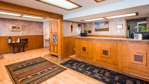 A reception area with a wooden reception desk, a coffee machine, and a microwave. There is a rug on the floor and a framed picture on the wall. - Deadwood Miners Hotel (Deadwood)