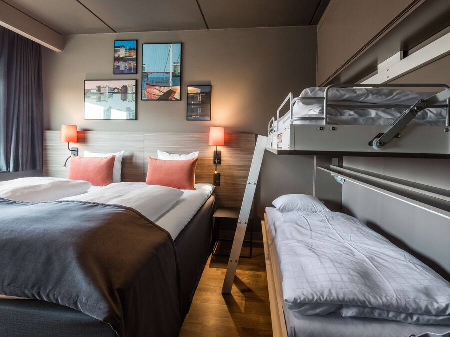 Habitación de hotel con dos camas, una litera, cabecero de madera y lámparas fijadas a la pared.