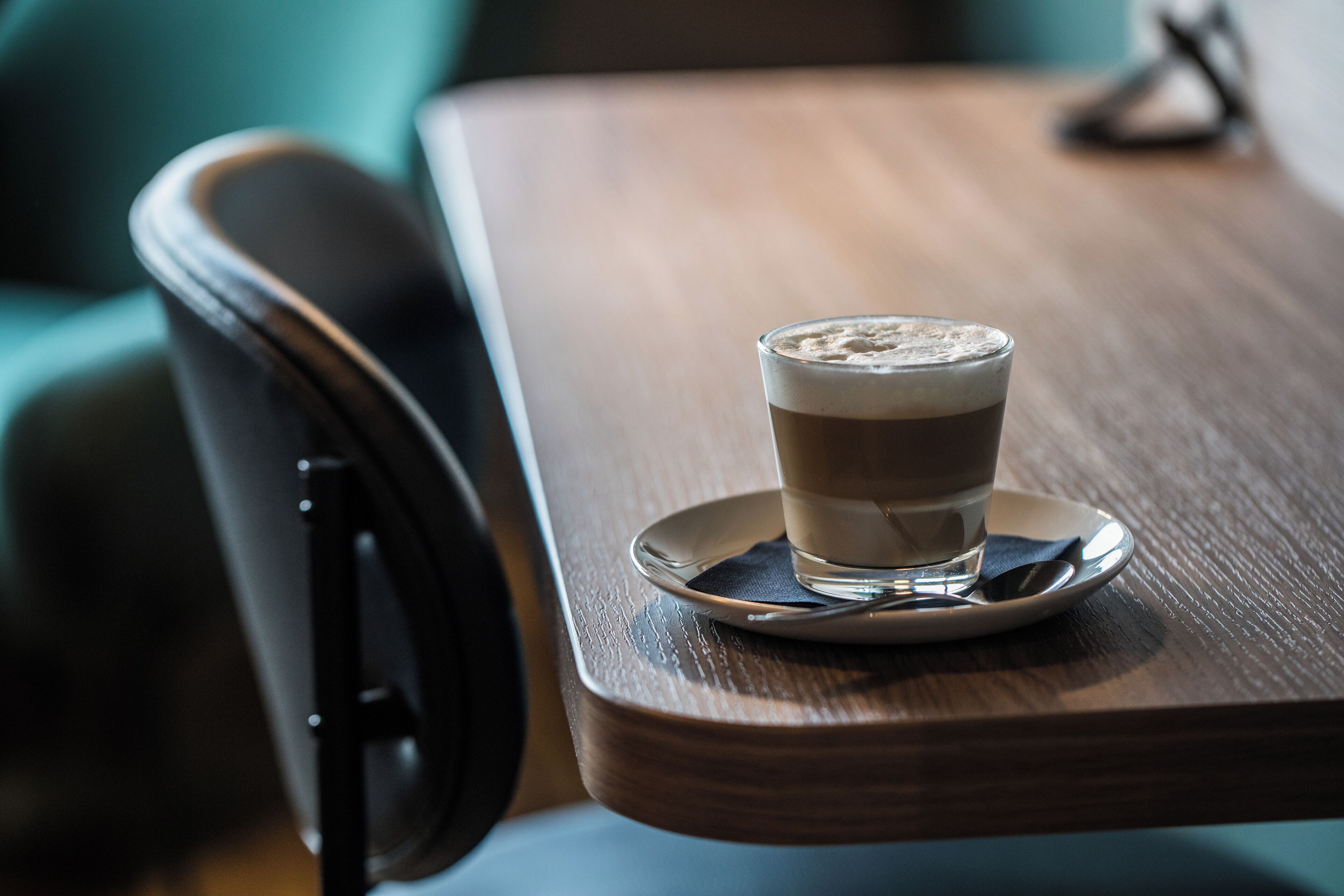 A wooden table with a glass of coffee on a saucer.