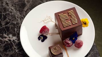 Un postre sobre un plato blanco con chocolate, frambuesas y flores.
