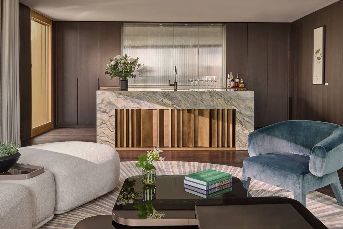 A modern living room with a sofa, a coffee table, and a blue chair. There is a kitchen area with a marble countertop and a sink.