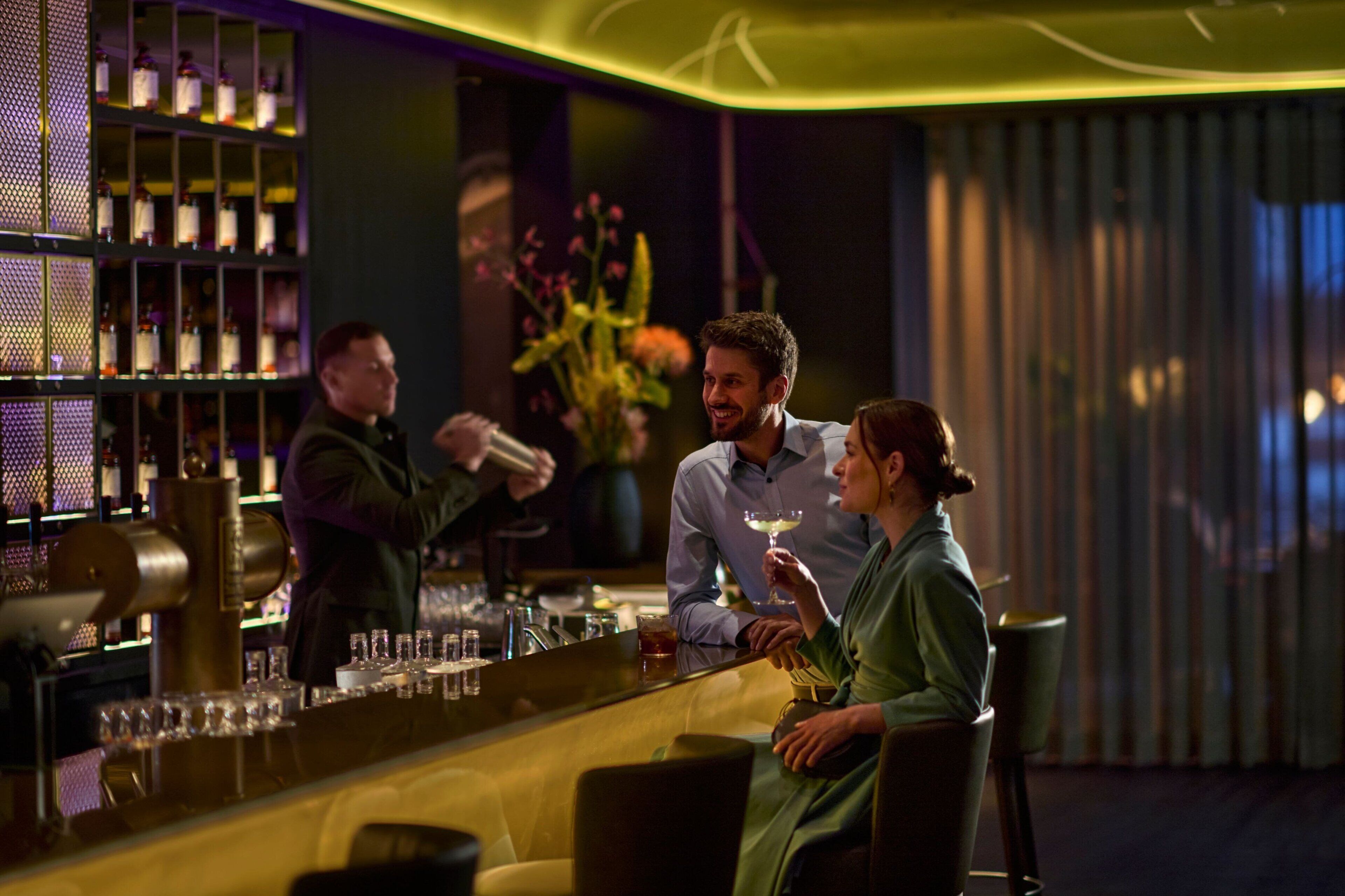 A bar area with a bartender, a customer holding a drink, and another customer seated.