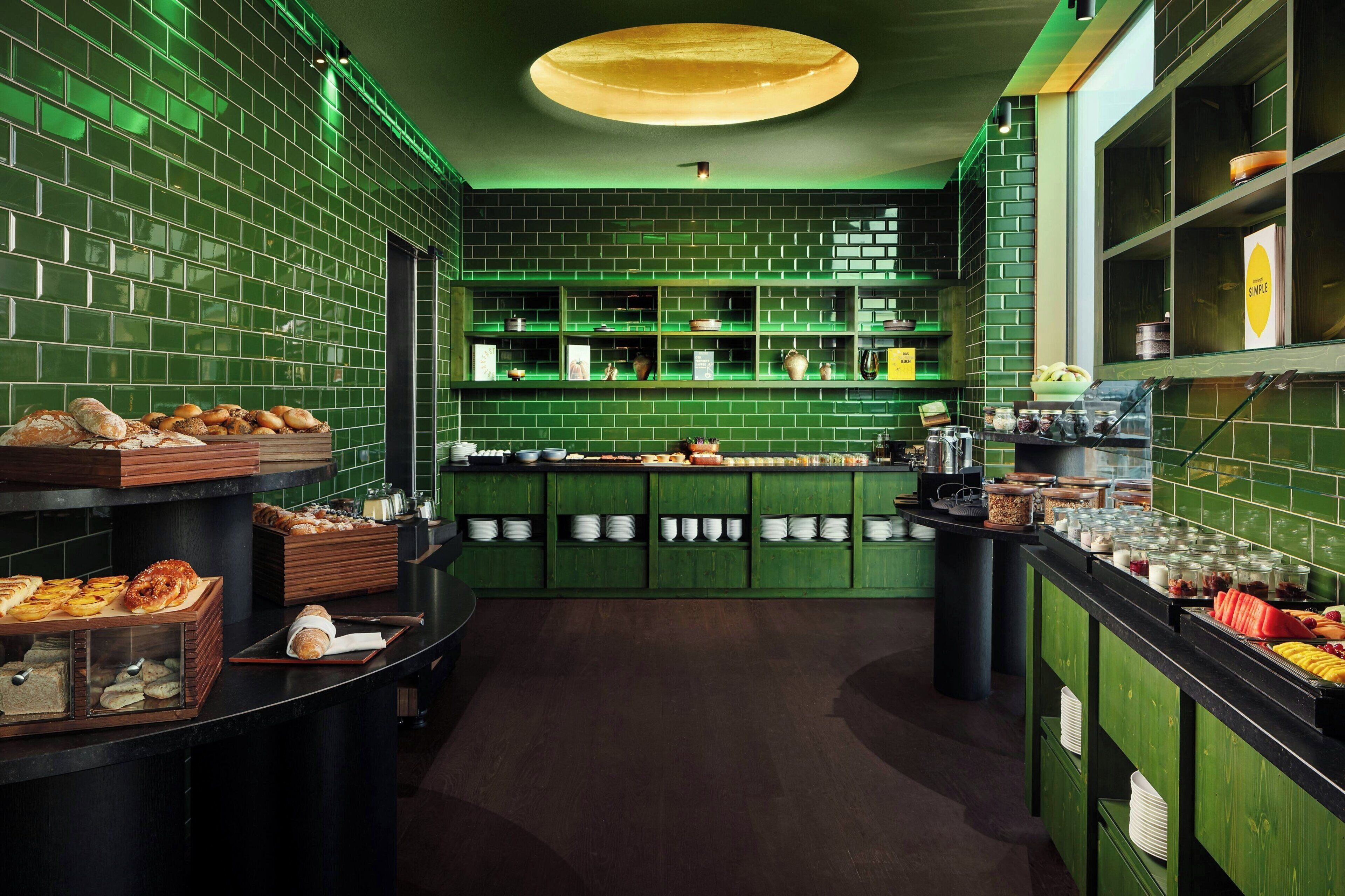 A restaurant with a green-tiled wall, a central counter with food displays, and a dark wooden floor.