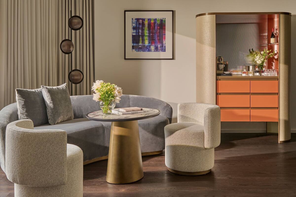 A modern living room with a grey sofa, round coffee table, and two armchairs. A bookshelf with books and decorative items is visible in the background.