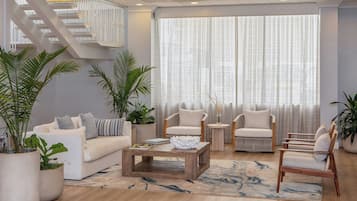 A modern living room with a staircase, white sofas, wooden coffee table, and potted plants.