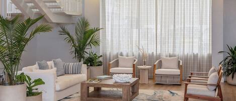 A modern living room with a staircase, white sofas, wooden coffee table, and potted plants.