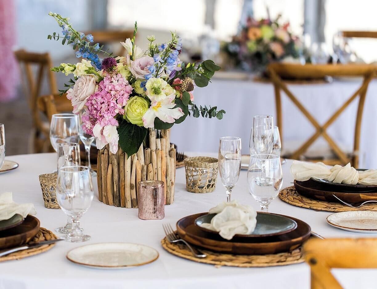 Une table dressée avec des assiettes, des verres et un centre de table composé de fleurs dans un vase rustique.