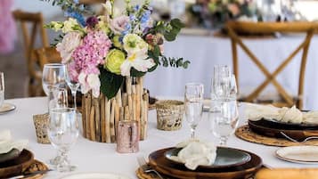 Une table dressée avec des assiettes, des verres et un centre de table composé de fleurs dans un vase rustique.