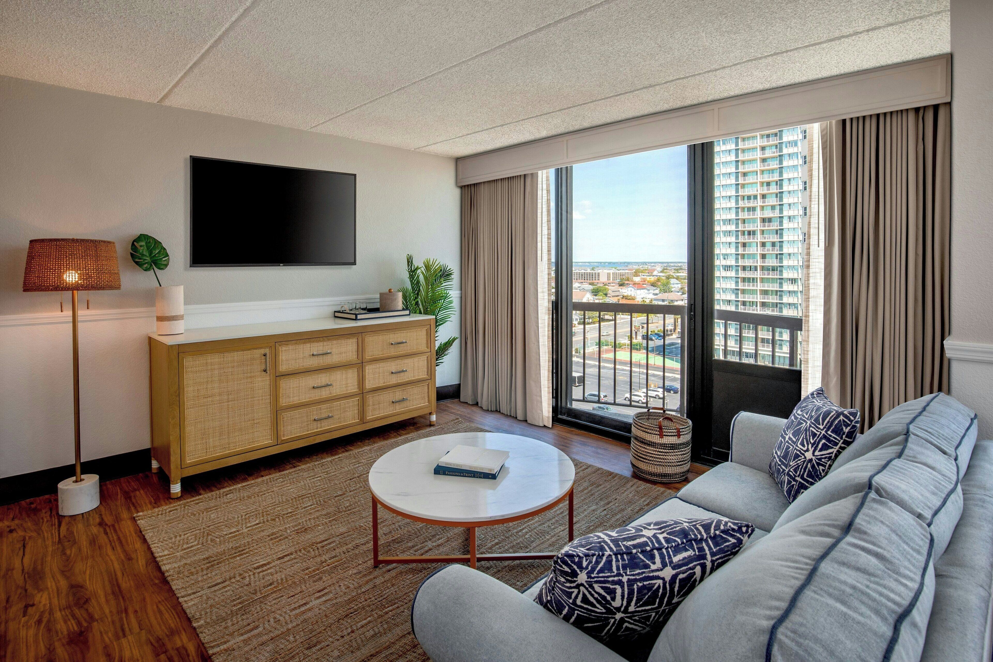 Una sala de estar moderna con un sofá, una mesa de centro, un televisor, un aparador y un ventanal con vistas a edificios.