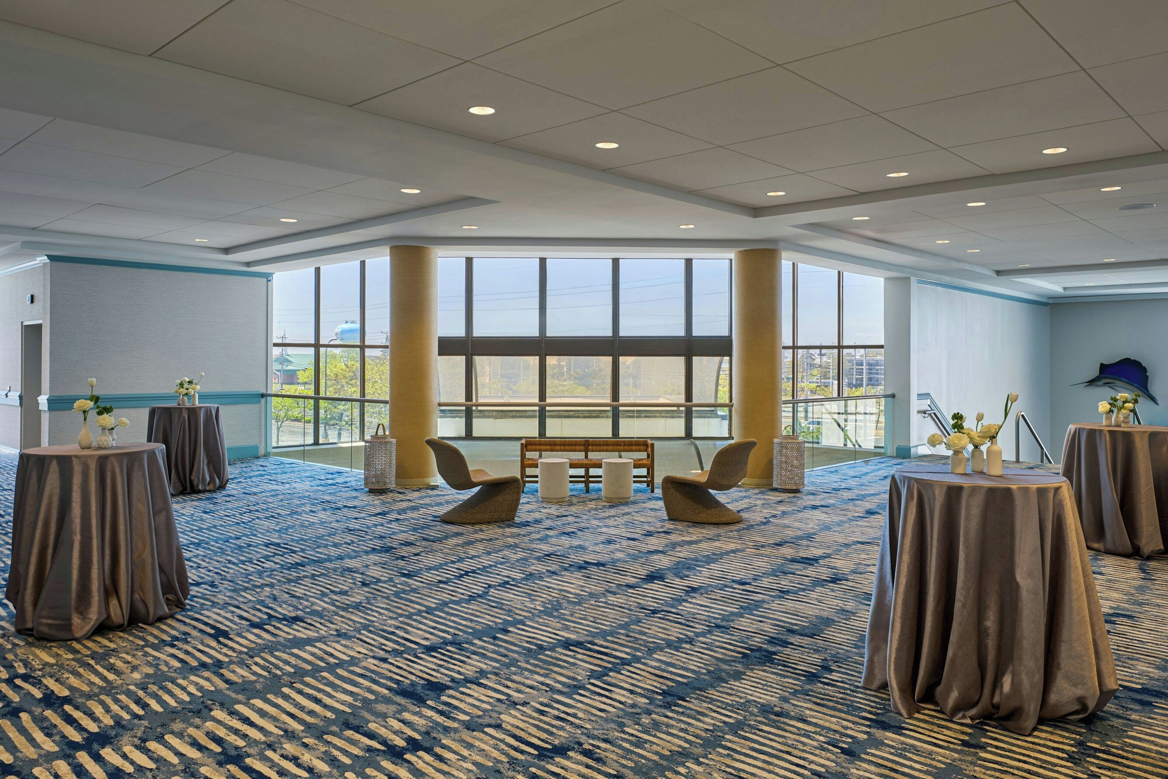 A spacious room with a patterned carpet, round tables with draped covers, and a large window offering a view of the cityscape.